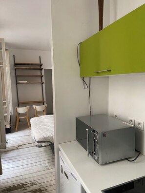 A room with a bed, a desk with a computer, a chair, a shelf, and a green partition. - Au Pied de la Butte Montmartre Avec Toutes Sortes de Commerces à Moins de 5 Mins (Paris)