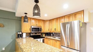 A kitchen with granite countertops, wooden cabinets, stainless steel appliances, and pendant lighting. - A-205 Enjoy Your Vacation In This Fabulous Remodeled Condominium! (Cabo San Lucas)