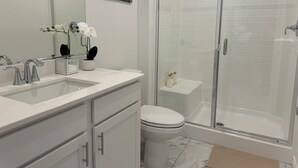 Un baño moderno con cabina de ducha de vidrio, un lavabo blanco con espejo y un inodoro.