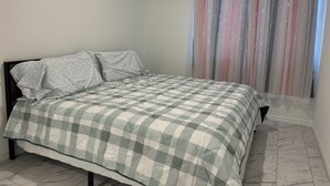 Una cama bien hecha con una colcha a cuadros, un almohadón y un cabecero.