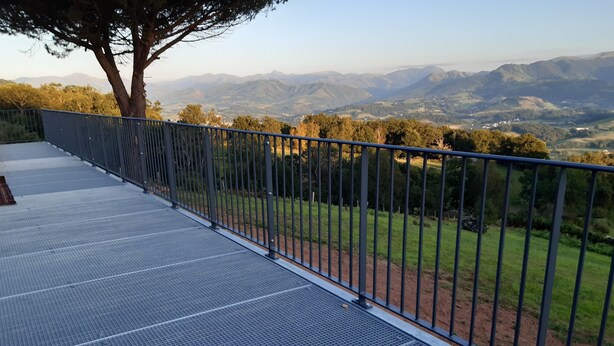 Une terrasse en métal avec une rambarde en métal, offrant une vue sur un paysage montagneux.