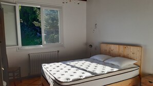 Une chambre avec un lit en bois, une fenêtre donnant sur un paysage verdoyant, un radiateur et un lustre.