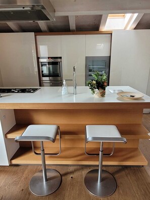 A modern kitchen with a central island, stainless steel appliances, and two bar stools.