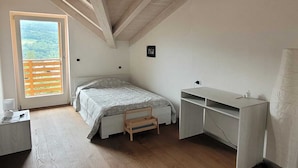 A bedroom with a bed, desk, and a window with a view of greenery. - Splendido Appartamento per il tuo Relax (Trentino-Alto Adige)
