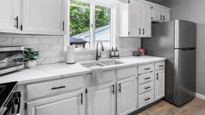 Una cocina moderna con armarios blancos, un refrigerador de acero inoxidable, un lavamanos doble y un ventanal con vistas al exterior.