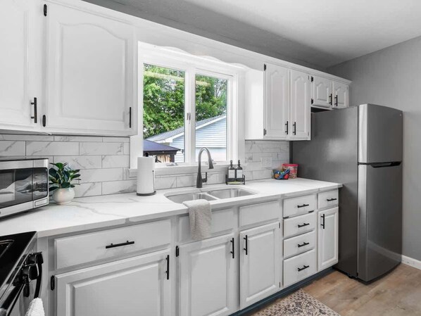 Una cocina moderna con armarios blancos, un refrigerador de acero inoxidable, un lavamanos doble y un ventanal con vistas al exterior.