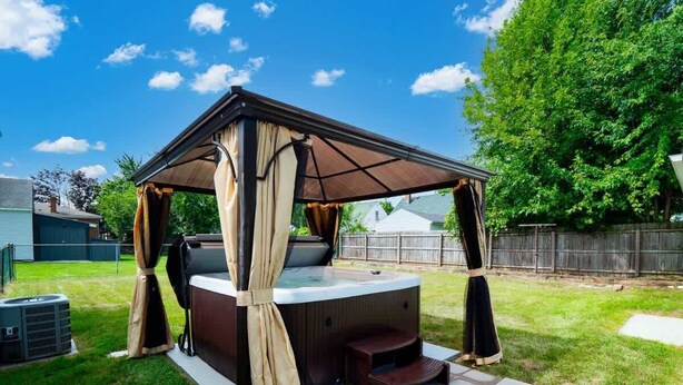 Un jacuzzi con toldo y escalones, rodeado por un jardín cubierto de césped.