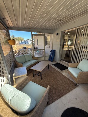 A covered outdoor seating area with wicker furniture, a small table, and a view of the backyard.