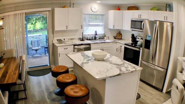 A modern kitchen with white cabinets, a marble island, stainless steel appliances, and a dining area with stools.