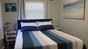 A neatly made bed with a striped bedspread, a bedside lamp, and a painting on the wall.