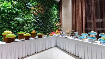 Montaje de bufé con diversos alimentos sobre una mesa, rodeado por un muro cubierto de verde exuberante.