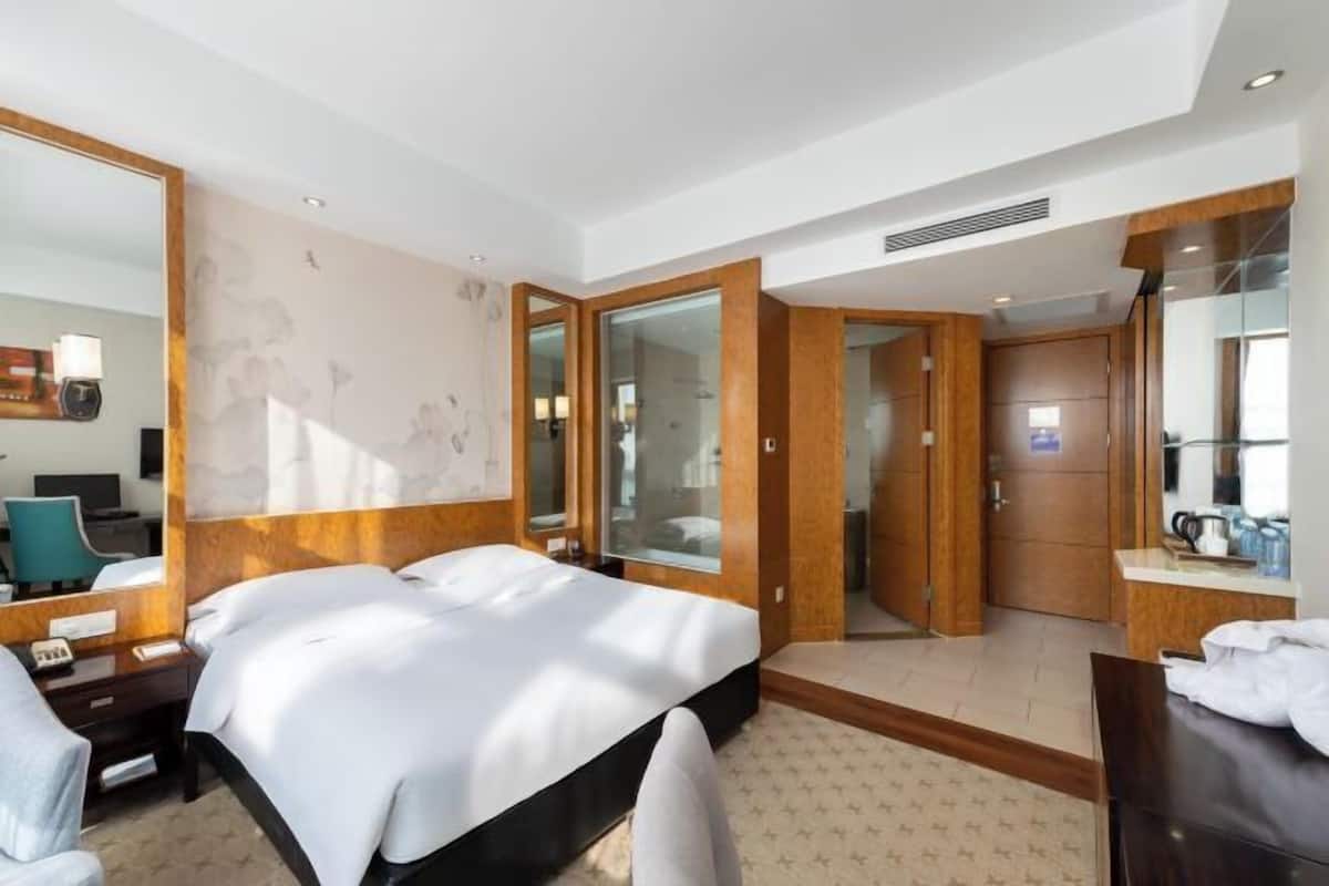 A hotel room with a large bed, a desk with a chair, a mirror, and a bathroom with a shower and toilet.