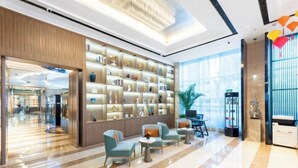 Eine moderne Hotellobby mit Marmorboden, einer großen Wandregal-Konstruktion mit Dekorationsobjekten und Sitzbereichen mit Tischen.