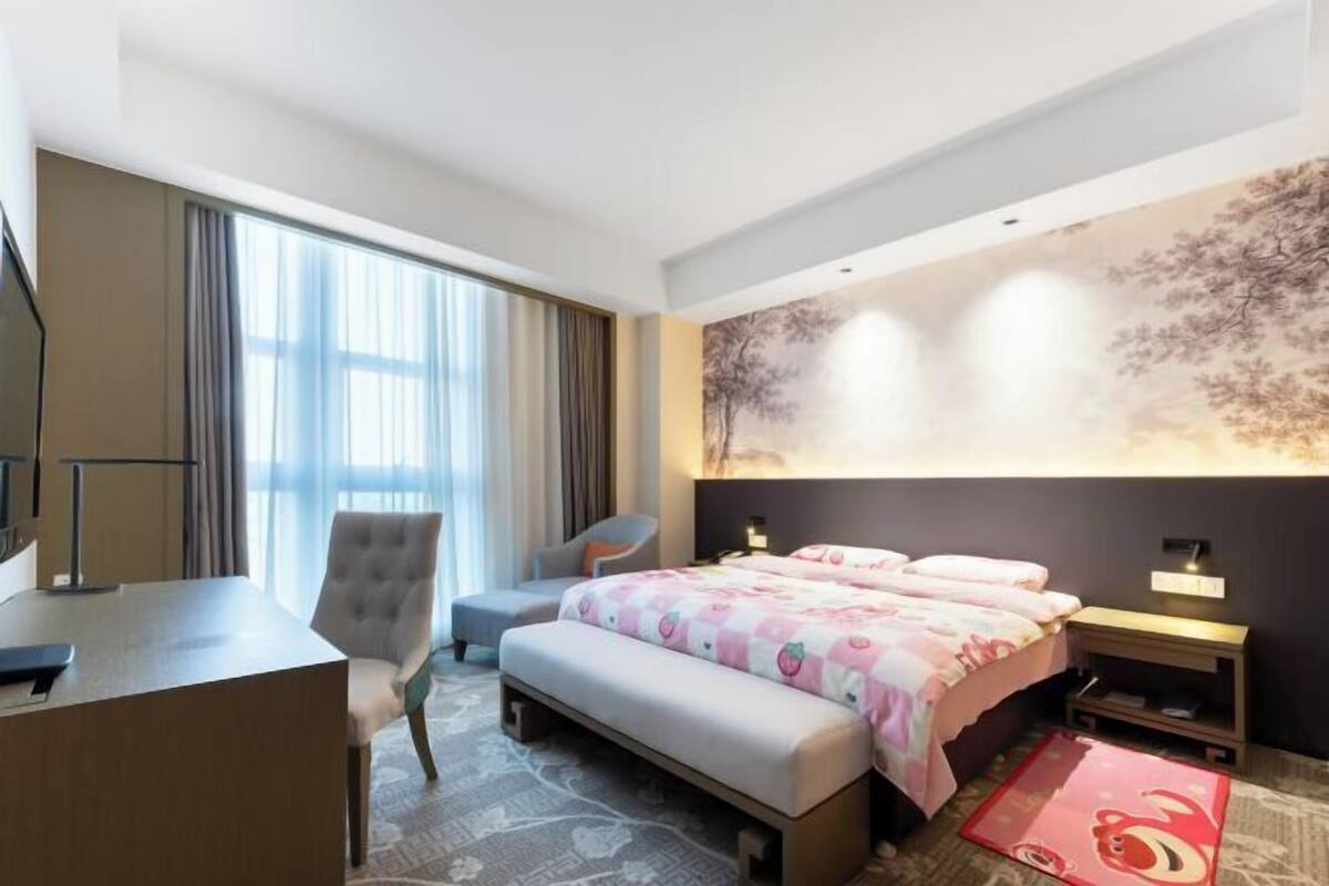 A hotel room with a bed, a desk, a chair, a large window, and a wall mural.