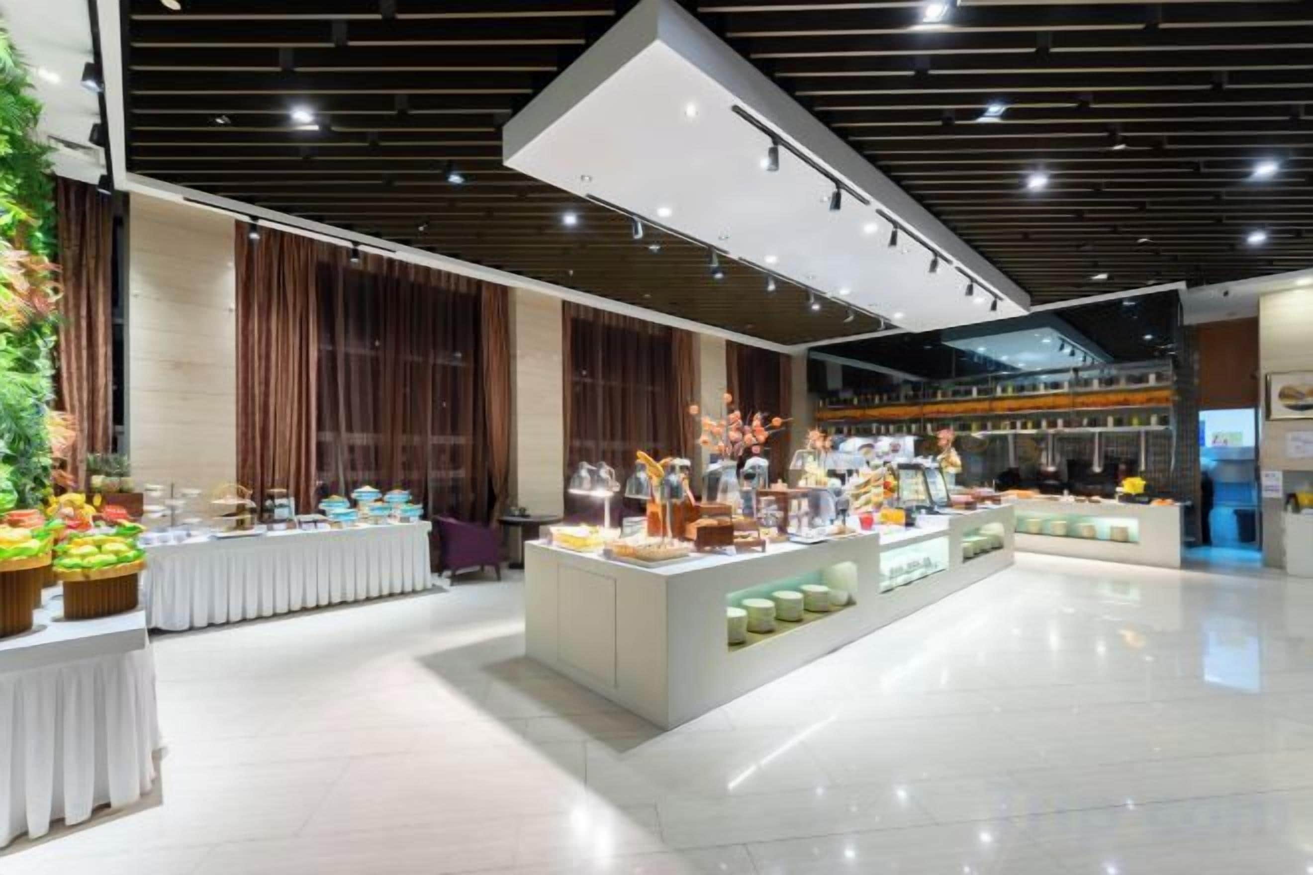 A spacious hotel lobby with a central island display, large windows, and a modern ceiling design.