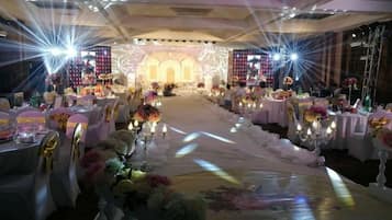 Un salón de banquetes con mesas redondas, centros de mesa florales y un escenario al frente.