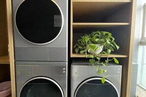 En kombinerad tvätt- och torkmaskin där maskinerna är staplade ovanpå varandra, och ovanpå dem finns en hylla med en krukväxt.
