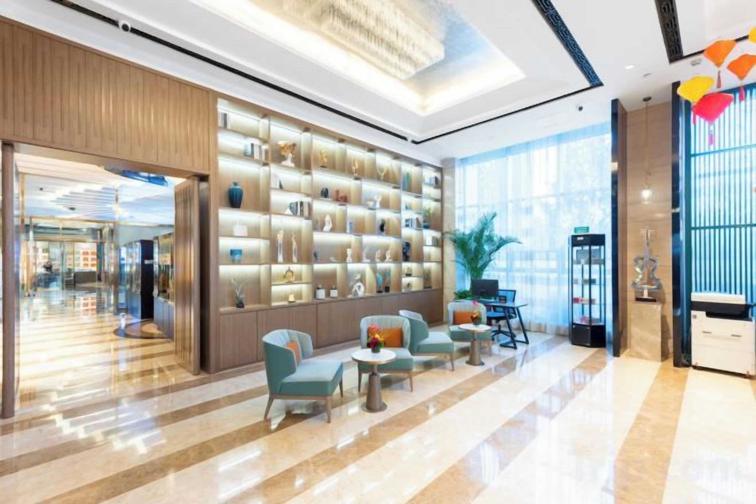 Een hotel lobby met een receptiebalie, een zithoek en een wand met decoratieve objecten.