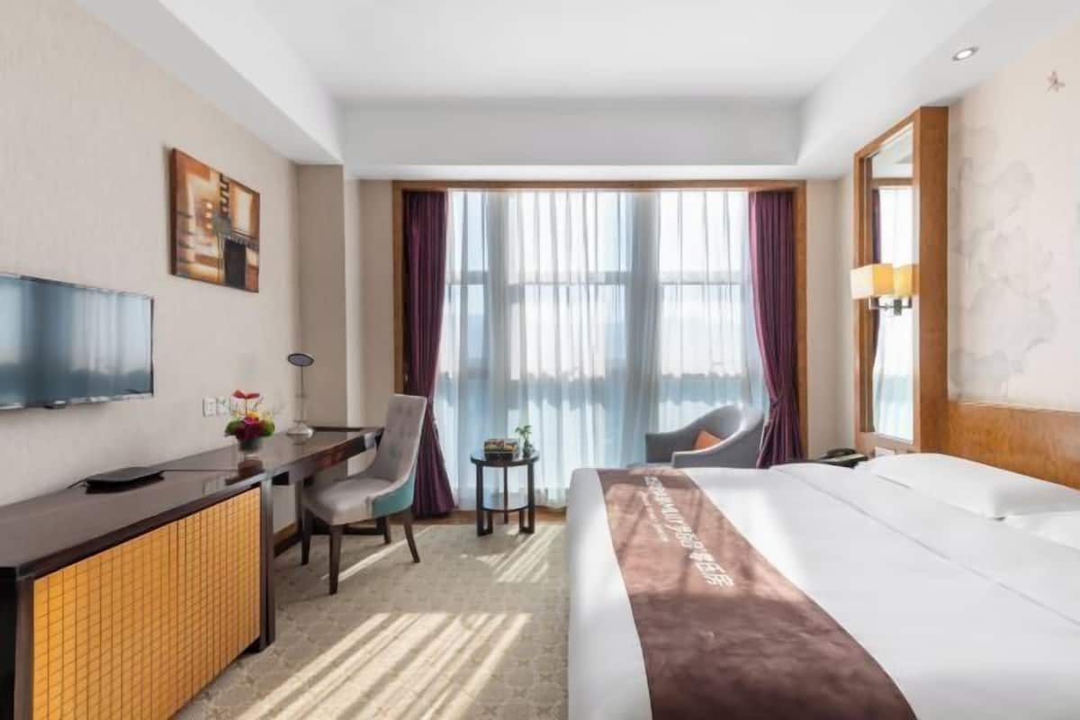 A hotel room with a bed, a desk, a chair, a TV, and a window with curtains.