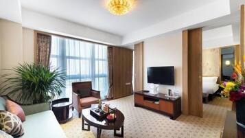 Una habitación de hotel con sofá, una mesa de centro, televisor y cama.