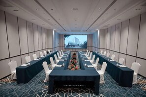 A conference room with a long table, white chairs, and a screen at the front. - Nishi Hotel (Jinan)