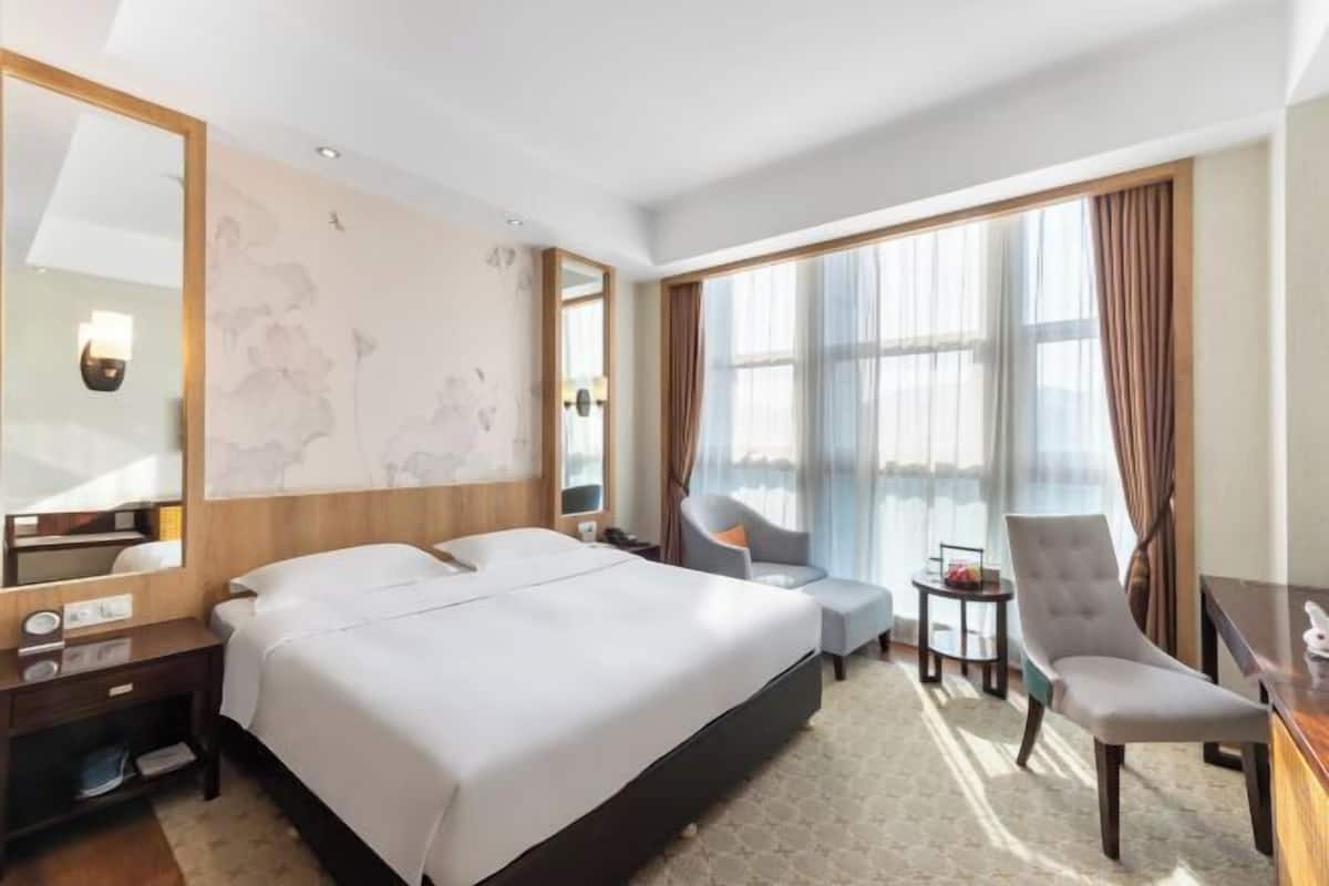 A hotel room with a large bed, a desk, a chair, and a small table.