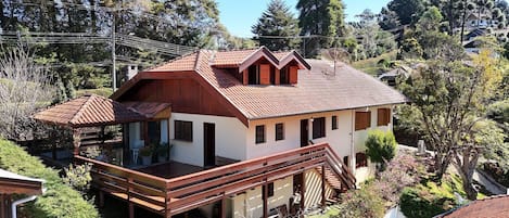 Una casa de dos pisos con un porche de madera, un patio cubierto y un pequeño jardín.