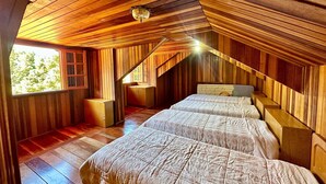 Une chambre confortable située sous les combles, avec des murs en bois et un plafond en pente, comprenant deux lits et une petite fenêtre.