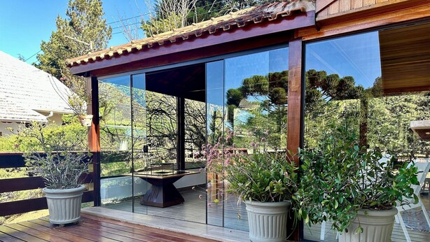 Une terrasse en bois agrémentée de plantes en pot, une véranda en verre et une vue sur le paysage environnant.