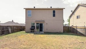 Une maison à deux étages avec une porte d’entrée, un petit patio et une clôture en bois.