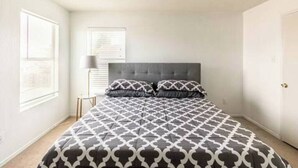 Une chambre à coucher avec un grand lit, une tête de lit et une fenêtre avec des stores.