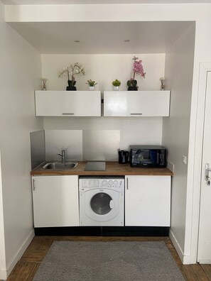 A compact kitchenette with a built-in washing machine, a microwave, and a sink.