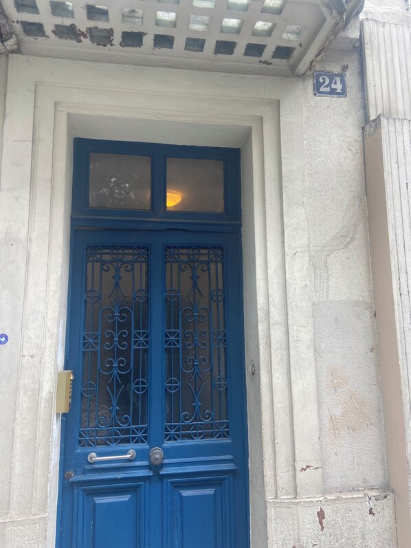 A blue door with a glass upper section and decorative metalwork, set in a building with a white facade and a number '24' sign.