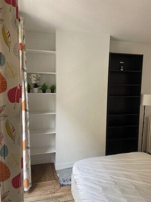 Une chambre à coucher avec un lit, une armoire, une étagère avec des plantes et un rideau orné de motifs de feuilles.