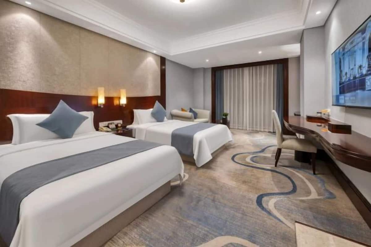 A hotel room with two beds, a desk, and a chair.