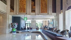 A spacious lobby with a curved reception desk, a Starbucks coffee machine, and a large window providing natural light. - Shaoxing Shangyu Radisson Wanjin Hotel (Shaoxing)