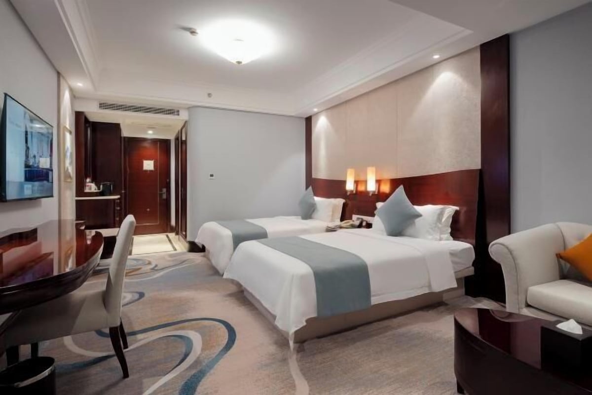 Habitación de hotel con dos camas, un escritorio, una silla, un televisor y un sofá.