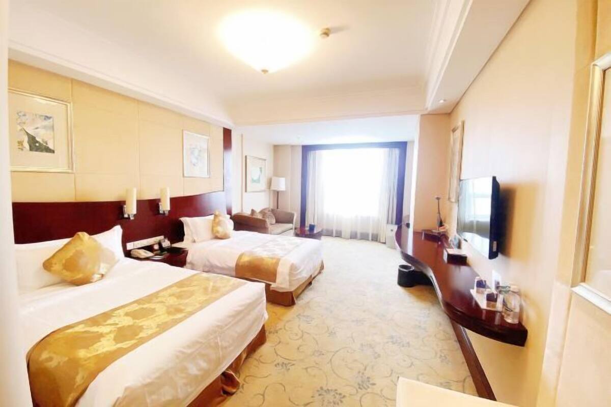 A hotel room with two beds, a desk, a TV, and a large window.