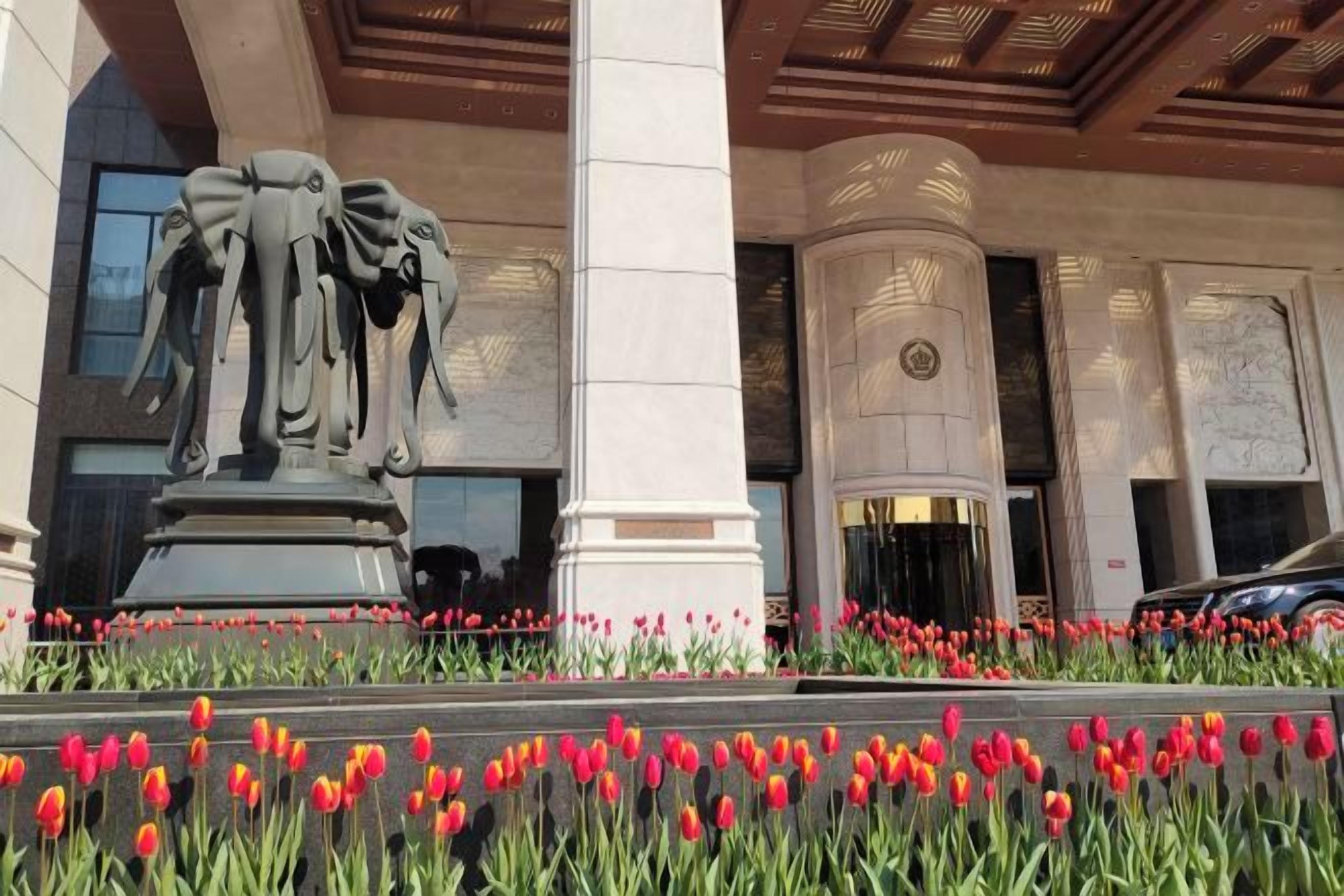 Eine Gebäudefassade mit einer zentralen Statue, Säulen und einem Blumenbeet mit roten Tulpen.