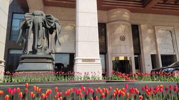 Eine Gebäudefassade mit einer zentralen Statue, Säulen und einem Blumenbeet mit roten Tulpen.