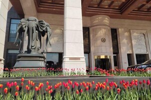 A building facade with a central statue, columns, and a flower bed with red tulips.