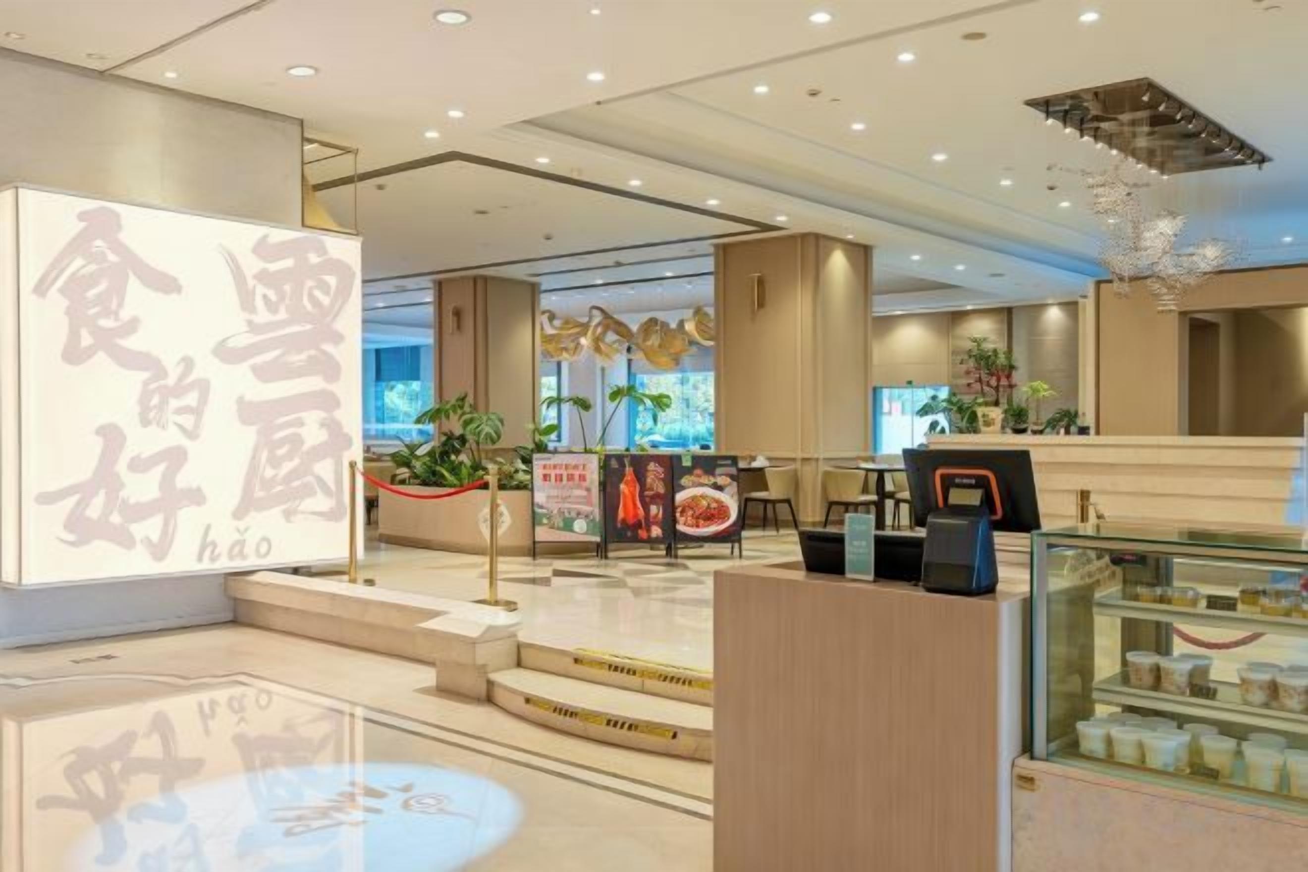 A modern interior with a reception desk, a digital menu board, and a display case with food items.