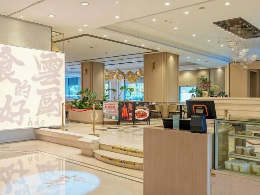 A modern interior with a reception desk, a digital menu board, and a display case with food items.