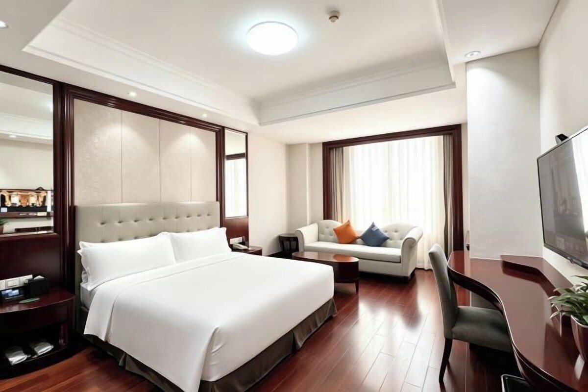 Una habitación de hotel con una cama grande, un sofá, un televisor y un escritorio.