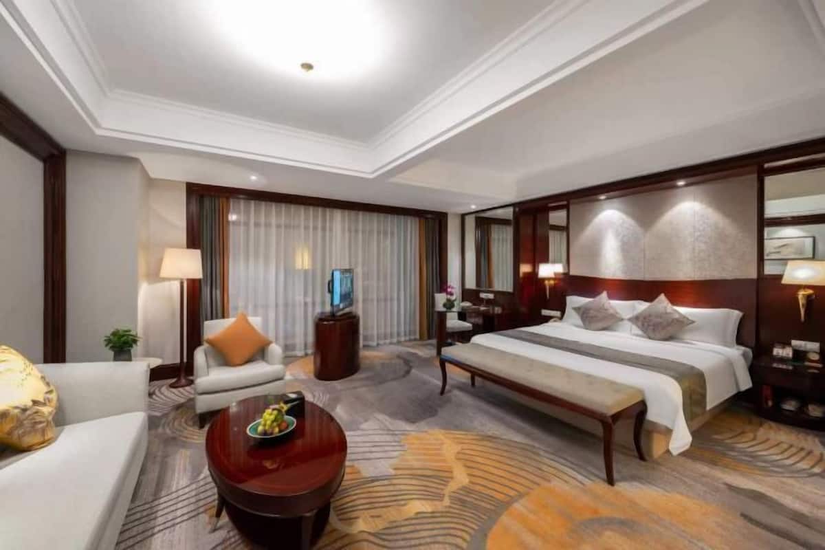 A hotel room with a bed, a sofa, a coffee table, a TV, and a large mirror.