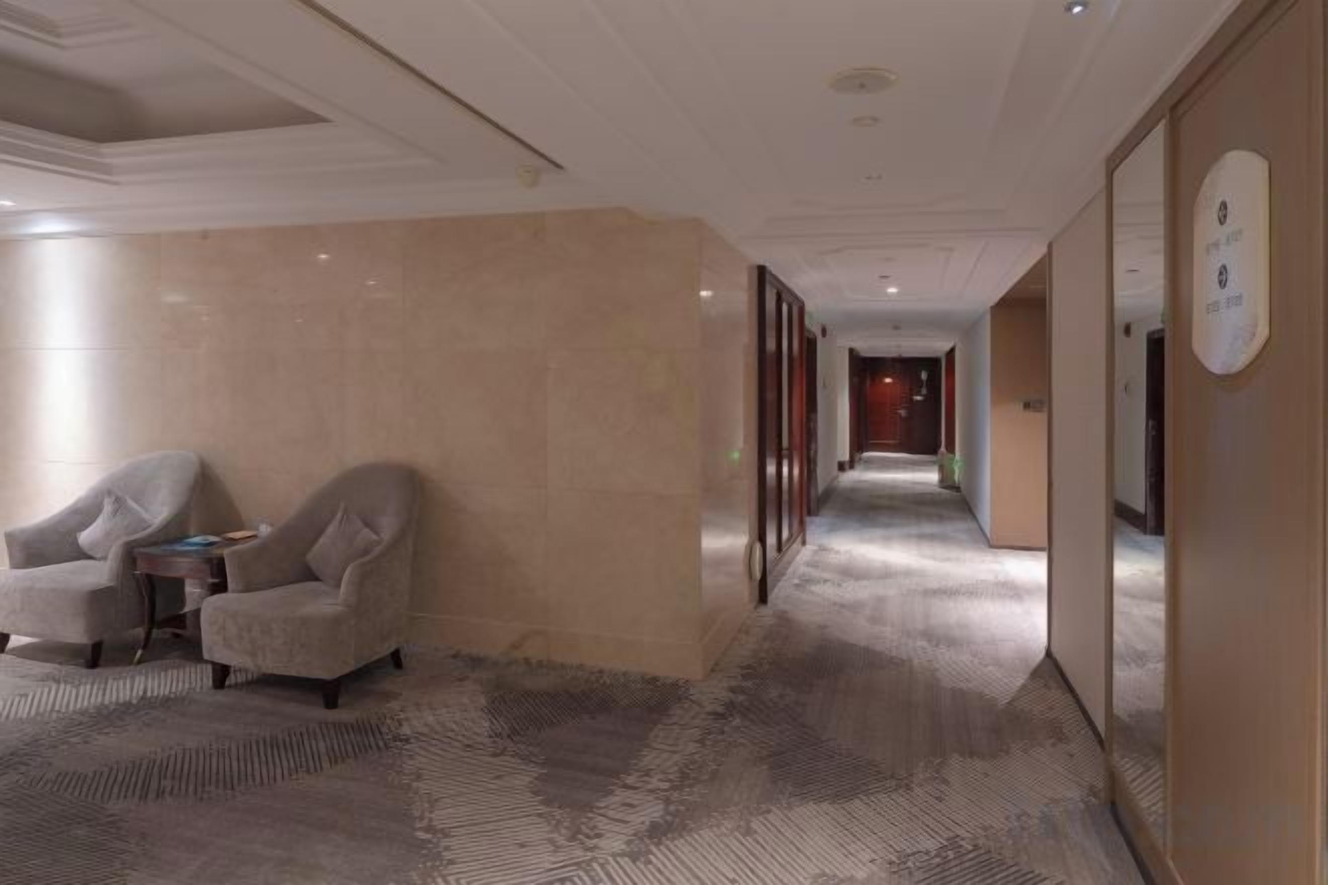 A hotel corridor with a carpeted floor, a seating area with two armchairs, and a wall-mounted sign.