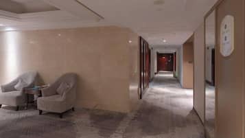 A hotel corridor with a carpeted floor, a seating area with two armchairs, and a wall-mounted sign.