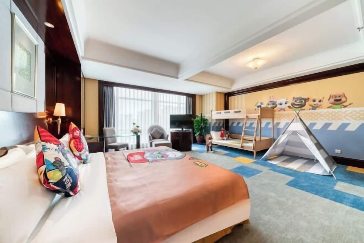 A hotel room with a bed, a desk, a chair, a TV, a window, a tent, and a wall with cartoon characters.