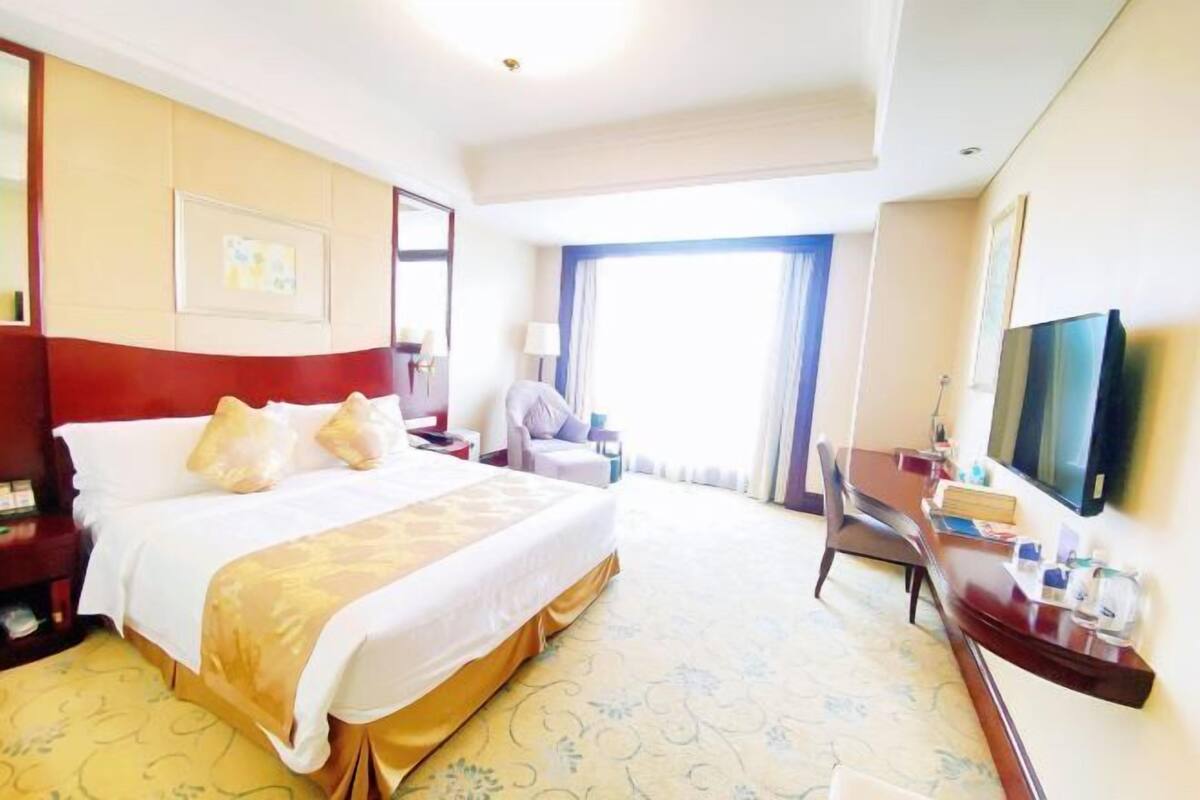 A hotel room with a bed, a desk, a chair, a TV, and a window.