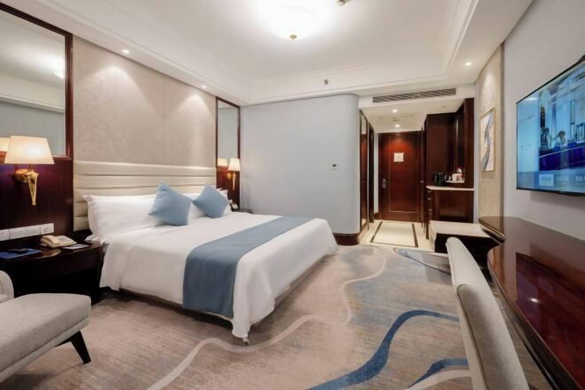 A hotel room with a large bed, a desk, a chair, a TV, and a bathroom visible through an open door.